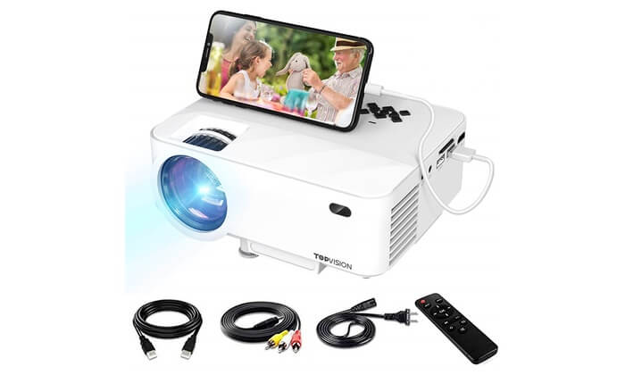 Top Vision Mini Projector in white with different black cords and remote below the projector. A cell phone sits on top of the projector. 